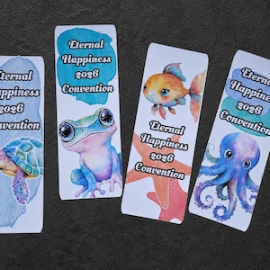 May include: Four rectangular bookmarks featuring watercolor illustrations of a sea turtle, a frog, a goldfish with a starfish, and an octopus. Each bookmark displays the text Eternal Happiness 2026 Convention in a black serif font over blue paint strokes.
