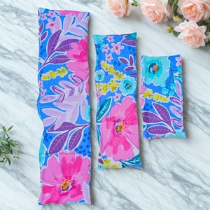 Peut inclure: Trois pochettes rectangulaires en tissu de longueurs variables pr&eacute;sentant un motif floral vibrant avec des fleurs et des feuilles rose vif, violettes, jaunes et bleu clair sur un fond bleu. Les pochettes sont cousues en segments.