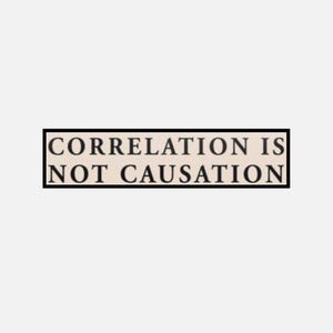 May include: A rectangular sign with a black border displays the text "CORRELATION IS NOT CAUSATION" in a serif font. The text is in black, set against a light beige background.