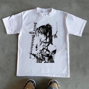 May include: White t-shirt featuring a black and white anime-style graphic of a person with the text "Saint Valentine's Day". The graphic includes a detailed illustration of a person with long hair and a choker. The shirt is made of a soft material.