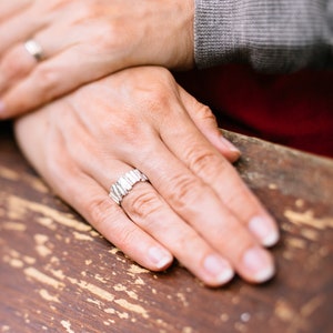 May include: A close-up of a person's hands wearing two silver rings. The person's hands are resting on a wooden surface.
