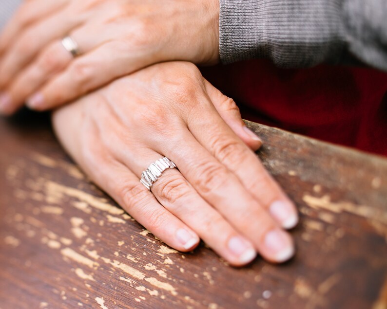 May include: A close-up of a person's hands wearing two silver rings. The person's hands are resting on a wooden surface.