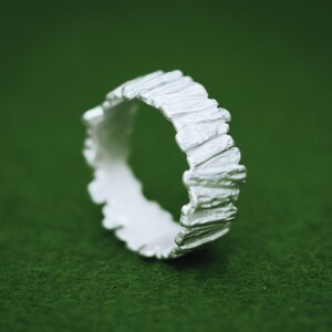 May include: A silver ring with a textured, organic design. The ring is made of a smooth, polished metal and has a unique, modern look.