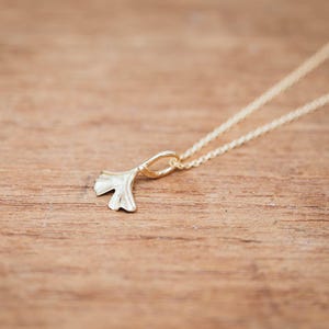 May include: A gold chain necklace with a delicate ginkgo leaf pendant. The pendant is a simple, elegant design.
