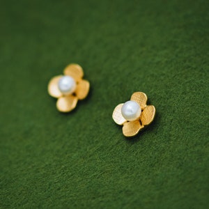 Peut inclure: Une paire de boucles d'oreilles en forme de fleur dorées avec une seule perle au centre de chaque fleur.