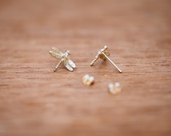 May include: A pair of gold dragonfly earrings. The earrings are small and delicate, with a detailed dragonfly design.