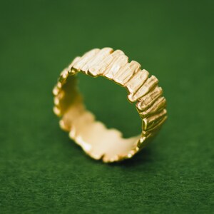 May include: A gold ring with a textured, organic design. The ring is made of a thick band of metal with a rough, uneven surface.