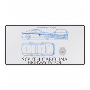 May include: A white rectangular mousepad featuring a blue blueprint of a 2023 Dodge Charger police car. The mousepad also includes the text "SOUTH CAROLINA HIGHWAY PATROL" and a badge.