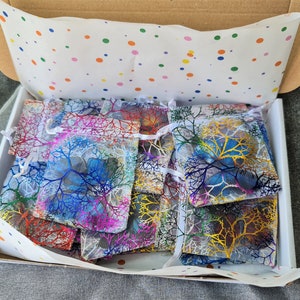 May include: A cardboard shipping box filled with multiple small, semi-transparent drawstring pouches. Each pouch features a colorful, branching, tree-like pattern in shades of blue, yellow, red, and purple. The box is lined with white tissue paper.