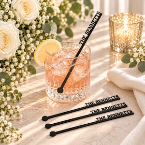 May include: A set of four black acrylic drink stirrers, each featuring the text THE BENNETTS in a bold, sans-serif font. One stirrer is placed inside a clear, textured glass filled with a pink beverage, ice, and a lemon slice.