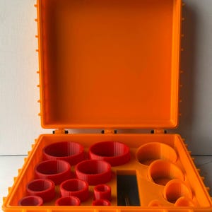 Peut inclure: Une boîte à outils orange ouverte avec une base grise, contenant divers objets circulaires rouges de différentes tailles. La boîte à outils est en plastique durable et possède un mécanisme de verrouillage sûr. L'intérieur est conçu pour contenir les objets rouges.