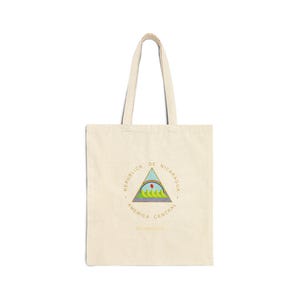 May include: Cream-colored tote bag with a Nicaraguan coat of arms design. The emblem features a triangle with a rainbow, mountains, and the words "REPUBLICA DE NICARAGUA" and "AMERICA CENTRAL" in a circular pattern.