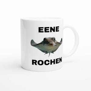 Può includere: Tazza in ceramica bianca con un disegno di una razza che fuma una sigaretta. Il testo "EENE ROCHEN" è stampato in nero sopra e sotto l'immagine della razza. La tazza ha un manico curvo.