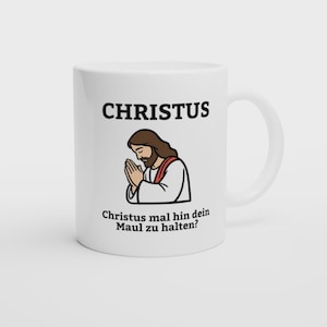 Könnte beinhalten: Ein weißer Keramikbecher mit einer grafischen Illustration einer Figur mit langem braunem Haar und Bart, die ein weißes Gewand mit einer roten Schärpe trägt und die Hände zum Gebet gefaltet hat. Der Text CHRISTUS steht oben, Christus mal hin dein Maul zu halten? steht unten.