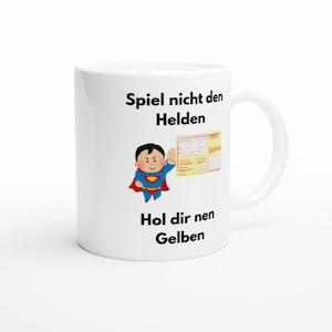 Könnte beinhalten: Ein weißer Keramikbecher mit einer Comicfigur in einem blau-roten Superheldenkostüm mit Umhang. Die Figur zeigt auf einen gelben Krankenschein. Der Text lautet: Spiel nicht den Helden, Hol dir nen Gelben.