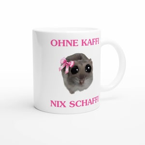 Puede incluir: Taza de cerámica blanca con un hámster de dibujos animados con un lazo rosa y ojos grandes. La taza tiene el texto "OHNE KAFFI" y "NIX SCHAFFI" en rosa. La taza tiene un asa curva.