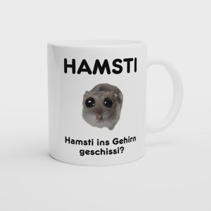 Op de afbeelding: Witte keramische mok met het woord "HAMSTI" in zwart, boven een cartoon hamster met grote ogen. Onder de hamster staat de zin "Hamsti ins Gehirn geschissi?" in zwart. De mok heeft een gebogen handvat.