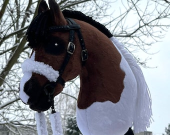 May include: A brown and white hobby horse with a black mane and bridle. The toy horse has a white muzzle and a long white tail. The stick horse is made of soft fabric and has a wooden stick.