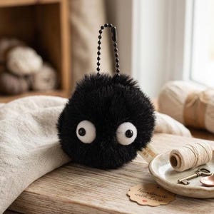 Cute soot sprite amigurumi plush keychain, perfect as an anime gift for her, presented in a clean, minimalist studio setting to highlight the soft materials.
