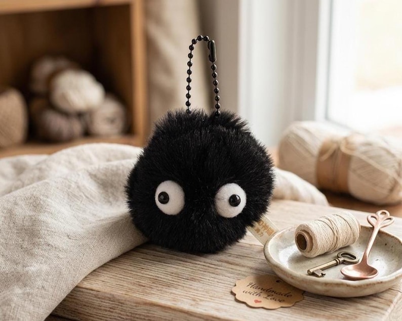 Cute soot sprite amigurumi plush keychain, perfect as an anime gift for her, presented in a clean, minimalist studio setting to highlight the soft materials.