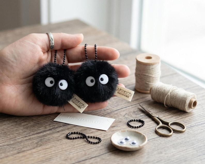 Detailed close-up of a handmade black dust spirit keychain with large white googly eyes and a soft faux-fur texture, showing the high-quality craftsmanship