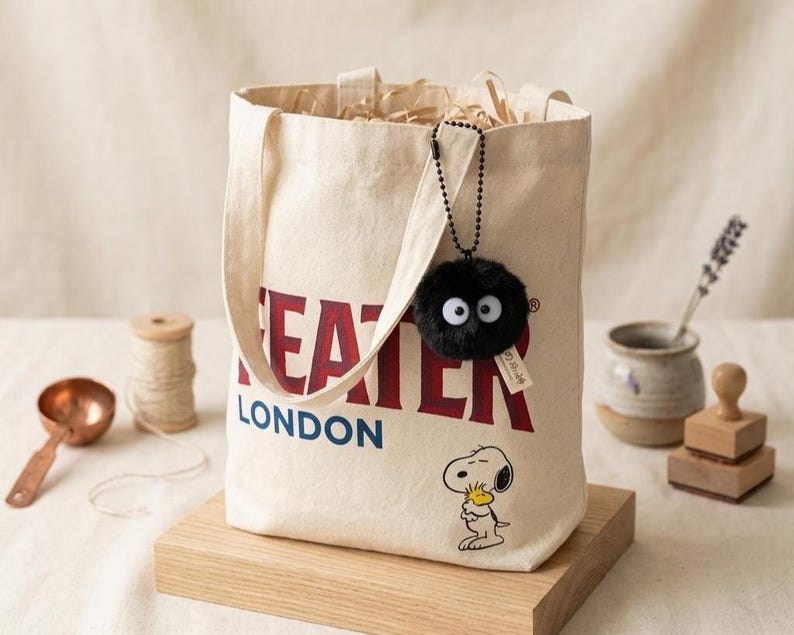 Black soot sprite keychain with a silver ball chain, styled next to a ceramic dish and dried lavender to emphasize the kawaii aesthetic and gift-ready presentation