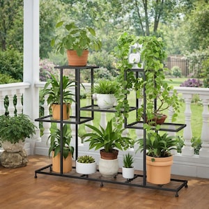 May include: A black metal plant stand with multiple shelves, displaying various potted plants. The plants include ferns, succulents, and other greenery in terracotta, white, and patterned pots. The stand is on a wooden deck with a white railing and a green background.