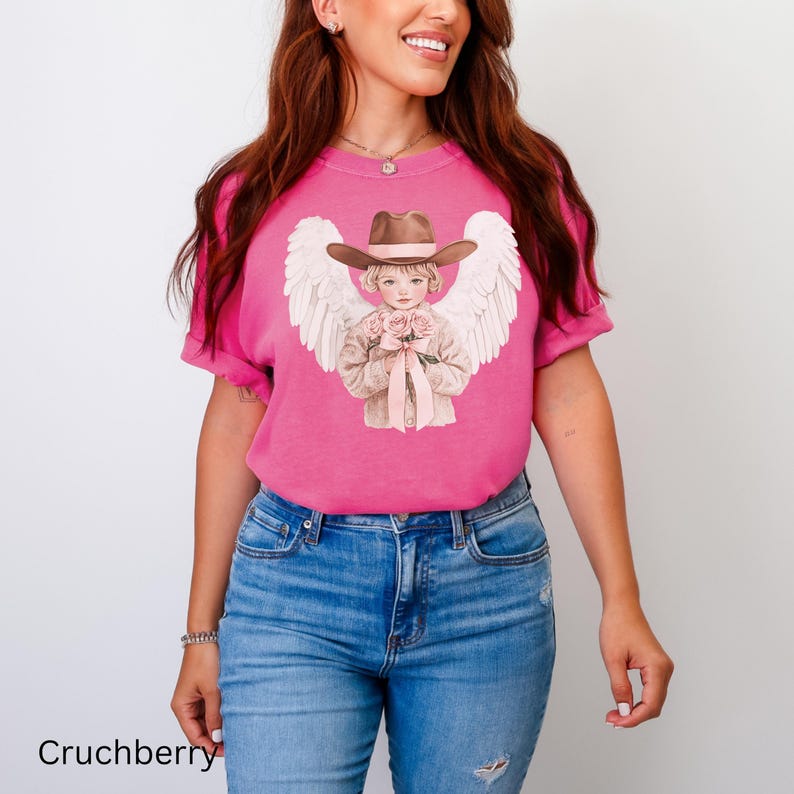 May include: A cerise t-shirt with a graphic of an angel in a cowboy hat, holding roses, and with white wings. The text "Cruchberry" is printed at the bottom of the shirt.
