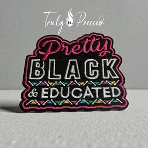 May include: A black embroidered patch with the words "Pretty BLACK & EDUCATED" in white and pink lettering. The patch has a pink border and colorful accents. The brand name "Truly n Pressed" is at the top.