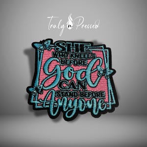 May include: Embroidered patch with the text "SHE WHO KNEELS BEFORE GOD CAN STAND BEFORE ANYONE" in teal and black on a pink background. The patch has a black border and butterfly accents.