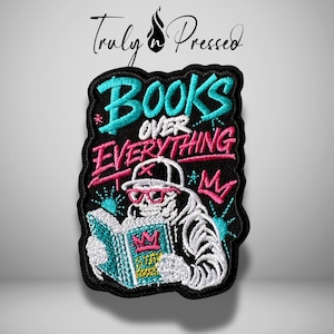 May include: Embroidered patch with the words "BOOKS OVER EVERYTHING" in turquoise and pink. The patch features a skeleton wearing a hat and glasses, reading a book. The patch is black with a decorative border.