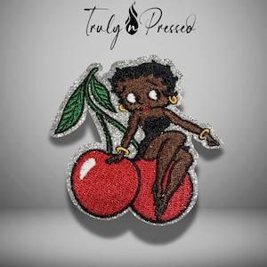 May include: Embroidered patch featuring a cartoon character sitting on a pair of red cherries with green leaves. The character is wearing a black dress and gold jewelry. The patch has a silver glitter border and the text "Truly Pressed" is at the top.