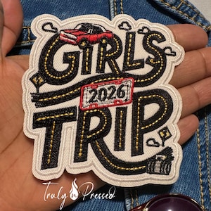 May include: Embroidered patch with the words "GIRLS TRIP 2026" in black, outlined in gold, and a red car graphic. The patch has a road design and a white border. The text "Truly n Pressed" is at the bottom.