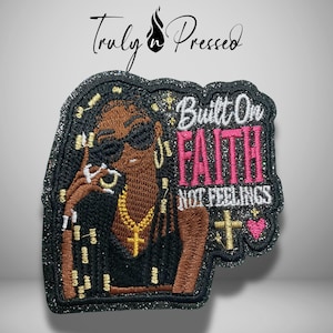 May include: A black glittery embroidered patch featuring a person with dark skin wearing sunglasses and a gold chain. The text reads Built On FAITH NOT FEELINGS in white and pink thread, accompanied by a gold cross and a small pink heart icon.