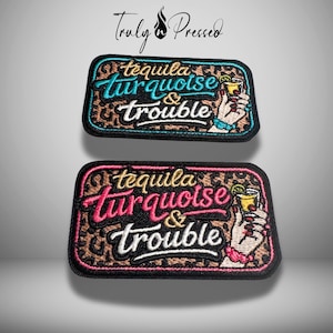 May include: Two embroidered patches with the text "tequila turquoise & trouble". The patches have a black border, leopard print background, and a hand holding a cocktail. One patch has turquoise text, the other has pink text.