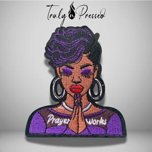 May include: An embroidered patch featuring a person with short purple hair, purple eyeshadow, and red lips, wearing large hoop earrings and a necklace. The person has hands pressed together in prayer, with the text Prayer Works embroidered in white.