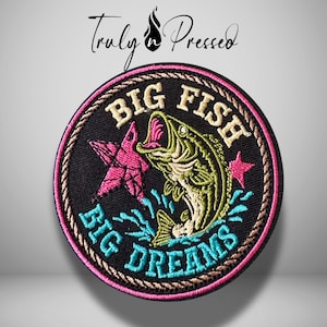 May include: A circular embroidered patch with a black background featuring a green fish jumping out of blue water splashes. It includes a pink star, the text BIG FISH in beige, and BIG DREAMS in bright blue. The border is pink and brown rope-style.