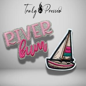 May include: Two embroidered patches. One patch features the text "RIVER bum" in pink thread with a silver glitter background. The second patch is a sailboat with a beige sail, a pink and teal striped section, and a pink hull with black outlines.