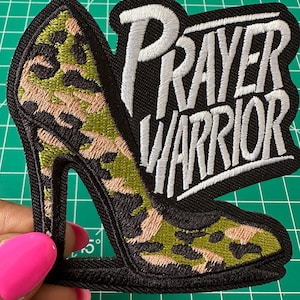 May include: An embroidered patch featuring a high-heeled shoe with a green, tan, and black camouflage pattern. The text "PRAYER WARRIOR" is stitched in white thread with a black background. The patch has a thick black border and measures over 3 inches.