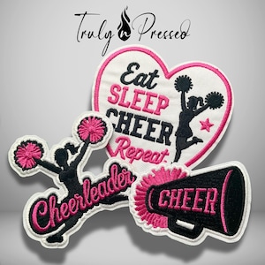 May include: Three embroidered patches featuring cheerleading themes. One heart-shaped patch reads Eat SLEEP CHEER Repeat with a black silhouette of a cheerleader. A second patch shows a cheerleader with pink pom-poms and the word Cheerleader. A third patch is a black megaphone with pink text reading CHEER.