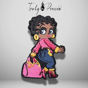 May include: An embroidered patch featuring a cartoon character with dark skin and black hair, wearing a pink long-sleeved top, blue jeans, and red high-heeled shoes. The character holds a large pink handbag and wears gold hoop earrings and bracelets.