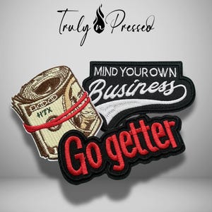May include: Three embroidered patches featuring a rolled stack of cash with a red rubber band, a black patch with white text reading "MIND YOUR OWN Business," and a black patch with red text reading "Go getter" against a light gray background.