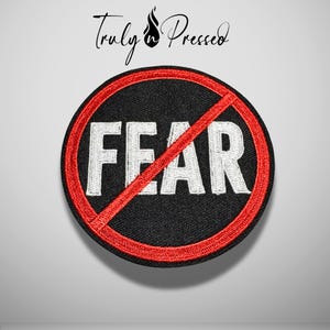 May include: A circular embroidered patch featuring a black background with the white text FEAR in capital letters. A red border circles the patch, and a red diagonal line crosses through the center. The text Truly n Pressed is above.