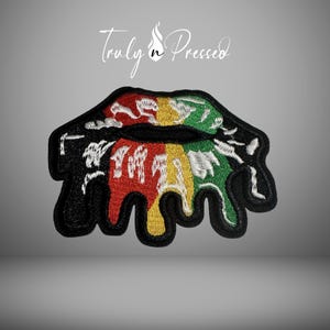 May include: Embroidered patch featuring a black outline of lips with a dripping design. The dripping design is filled with red, yellow, and green colors. The patch has the text "Truly n Pressed" in a script font.