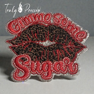 May include: Embroidered patch featuring a pair of red lips with a leopard print design. The words "Gimme Some Sugar" are embroidered in red with a silver glitter outline. The patch has a silver glitter border.