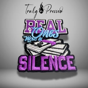 May include: Embroidered patch with the words "REAL ONES Move in SILENCE" in purple and light blue. The patch features a stack of books and the text "Truly Pressed" in cursive.