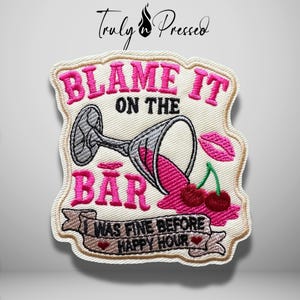 May include: An embroidered patch featuring a spilled martini glass with pink liquid, two red cherries, and a pink lip icon. The text reads BLAME IT ON THE BAR and I WAS FINE BEFORE HAPPY HOUR in pink and black thread on a cream-colored background.