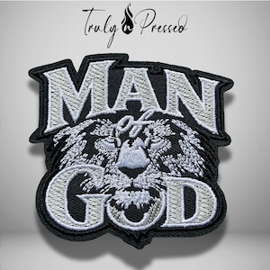 May include: A black and white embroidered patch featuring the text "MAN of GOD" in bold, capitalized letters. The design includes a detailed, stylized lion face centered between the words, all rendered in white thread against a black background.