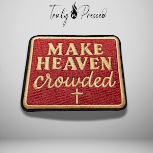 May include: A rectangular embroidered patch with a red background and a gold border. The text reads MAKE HEAVEN crowded in gold thread, with a small gold cross symbol centered below the text. The patch has a black stitched edge finish.