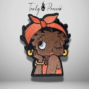 May include: An embroidered patch featuring a cartoon character with dark skin, black hair, and a red patterned headscarf. The character has one eye open, wears gold hoop earrings and a gold bracelet, and has red lips. The text Truly Pressed is above.